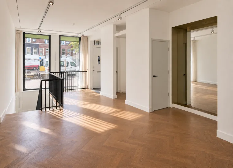 Finished impression across the empty herringbone-floor room towards the staircase and entrance